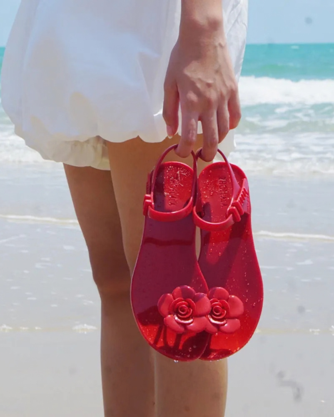 Red floral ZHOELALA sandals by the ocean.